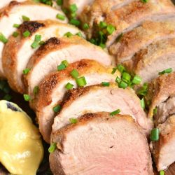 two pork tenderloins sliced and stacked on a cutting board with a spoon of mustards.