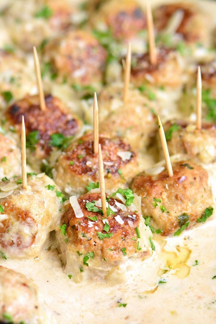 several garlic parmesan turkey meatballs in sauce with toothpicks.