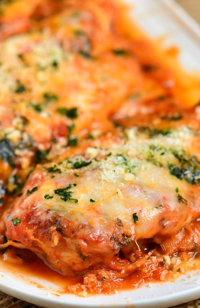 cheesy chicken breasts on the plate covered in spaghetti sauce, cheese, and herbs.