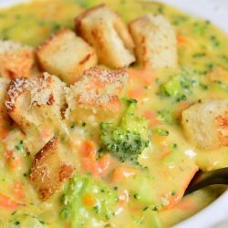 starting to spoon out some broccoli cheese soup topped with croutons.