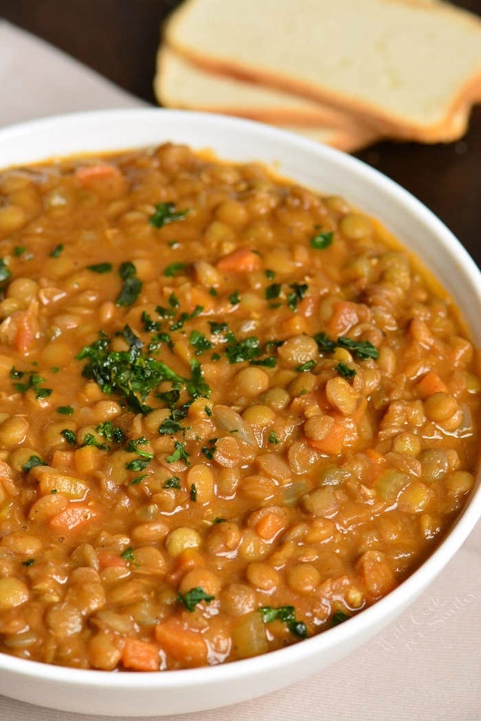 a white bowl filled with lentil soup and garnished with greens.