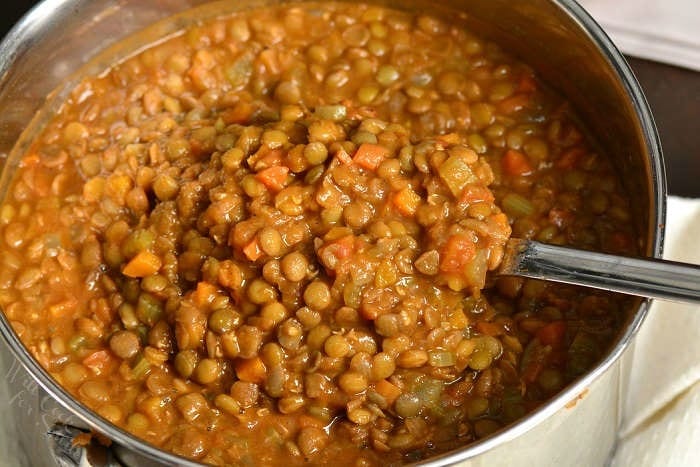 using a silver spoon to scoop out some lentil soup from the pot.