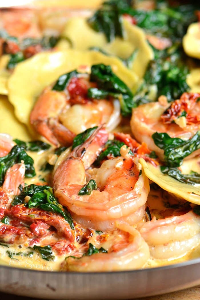 cooked ravioli with shrimp spinach and tomatoes all in creamy sauce in a pan.