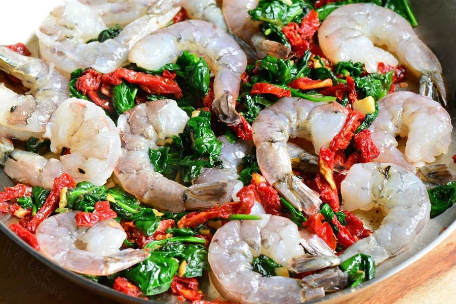 cooking shrimp in a skillet with spinach and tomatoes.
