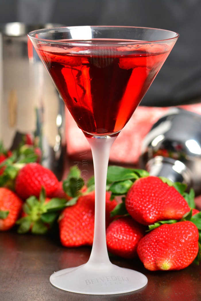 Strawberry Shortcake Martini in a martini in a martini glass on a wood table with strawberries around it