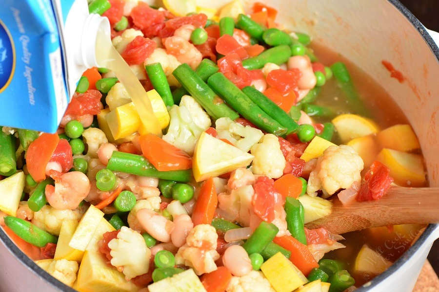 Bean and Vegetable Soup in a stock pot with chicken stock being poured in
