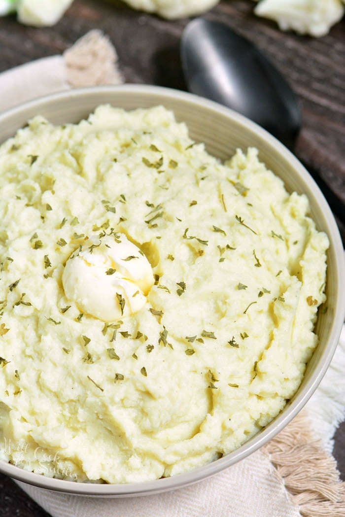 Mashed Cauliflower in a serving bowl with herbs and butter over top