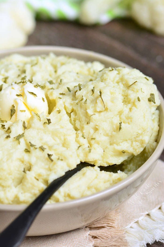 Mashed Cauliflower in a serving bowl with butter and herbs with a serving spoon