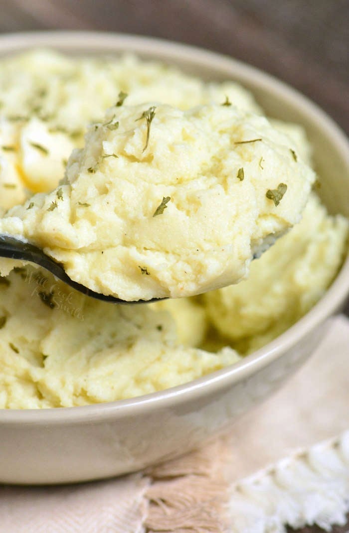 Mashed Cauliflower in a bowl being scooped up with a serving spoon