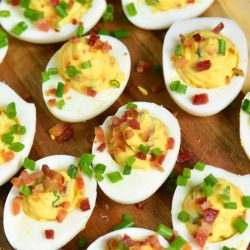 several creamy and smooth bacon deviled eggs with some chives on a wooden plate.