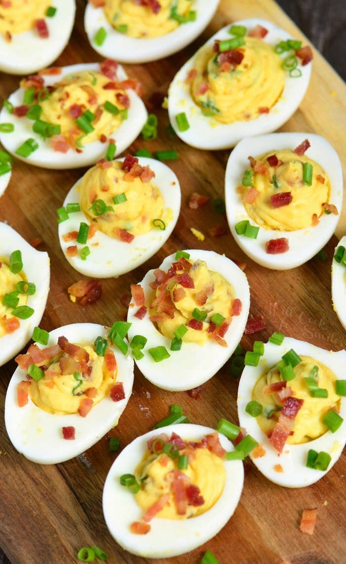 several creamy and smooth bacon deviled eggs with some chives on a wooden plate.