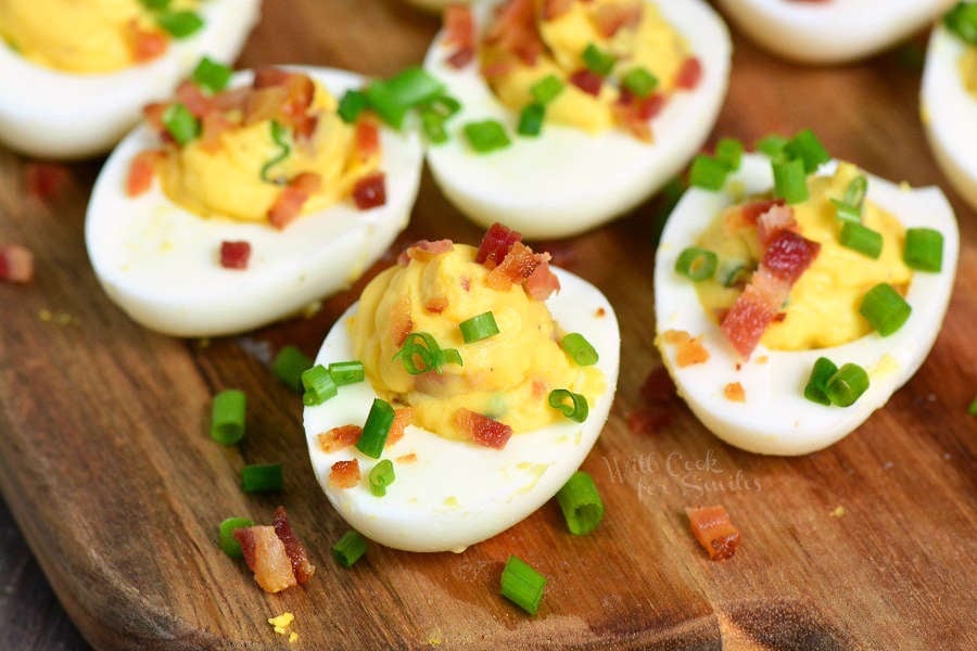 a few creamy deviled eggs with bacon and chives on the cutting board.