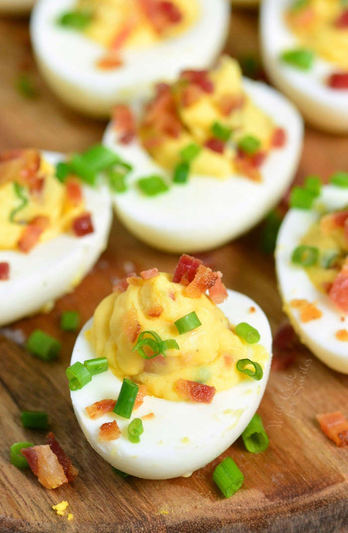 several creamy deviled eggs topped with bacon pieces and chives but focus on one.