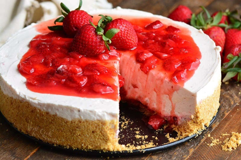 Strawberry No Bake Cheesecake with a slice missing on a wood table with strawberries