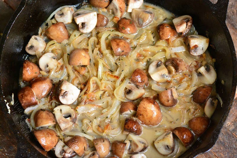 mushrooms and onions cooking in the skillet with broth and seasoning.