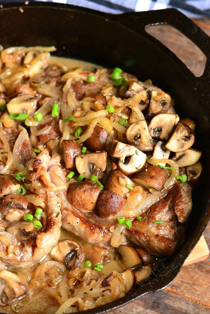 two large rib eye steaks in the skillet topped with sauce mushrooms and onions.