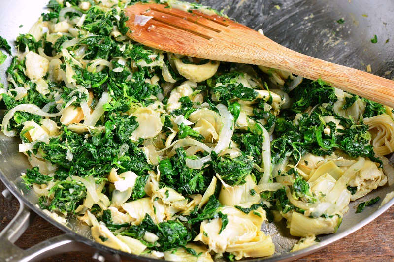 sauteed spinach and artichokes in a pan with a wooden spoon