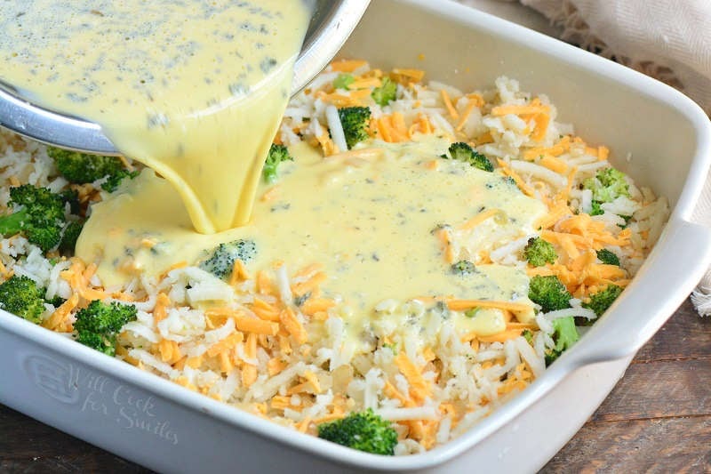 pouring in egg mixture into hashbrowns and broccoli and cheese in a baking dish.