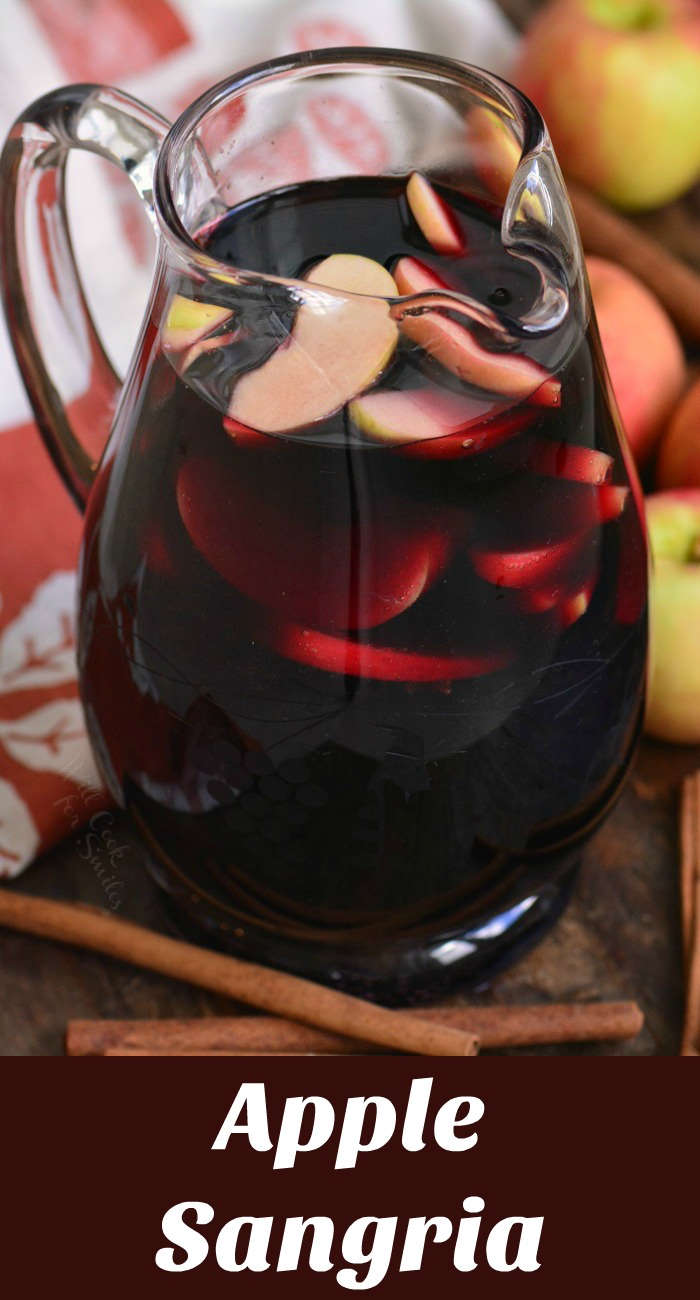 apple sangria in a pitcher on a wood cutting board with cinnamon sticks and apples