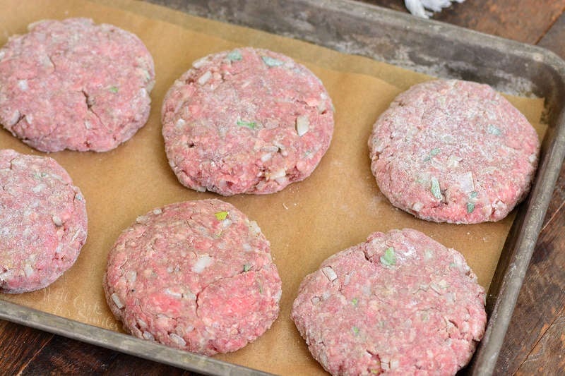 prepped and shaped raw Salisbury steak patties on parchment paper in a baking sheet.