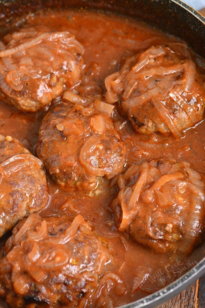 six Salisbury steak patties in the pan cooking in French onion sauce.
