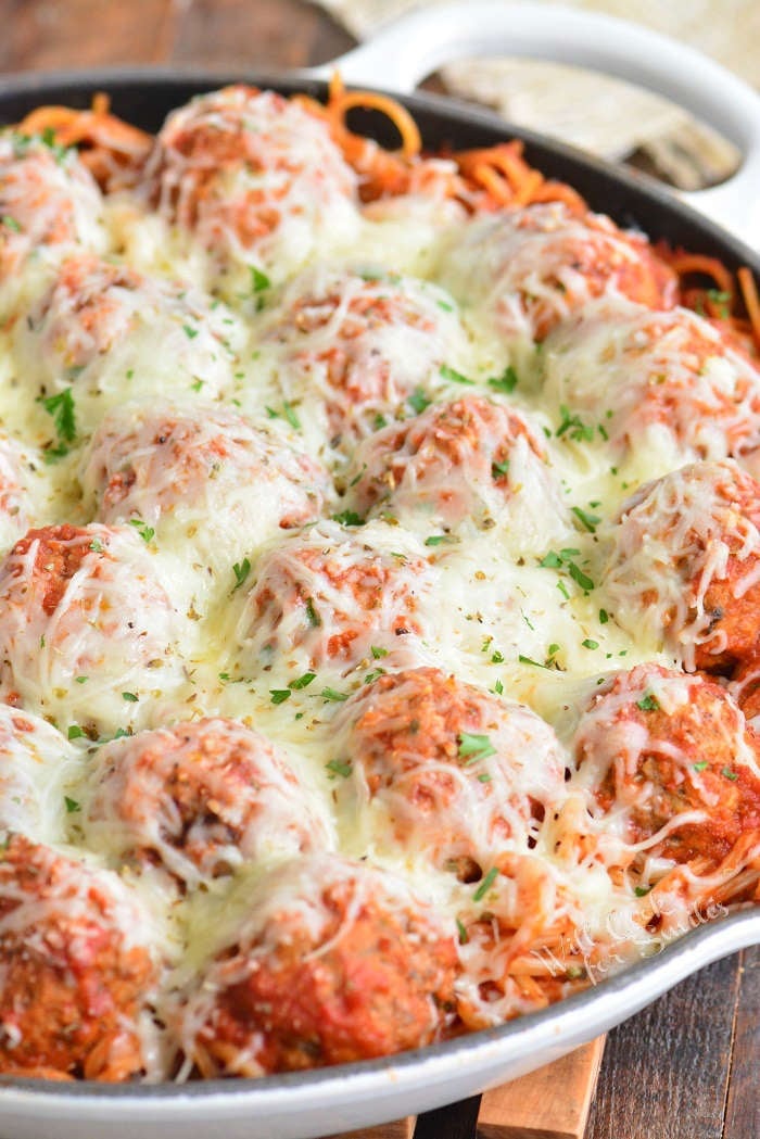 a skillet filled with baked pasta and meatballs and more cheese on top.