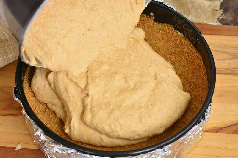 pouring filling into the cheesecake pan that is on a wood cutting board