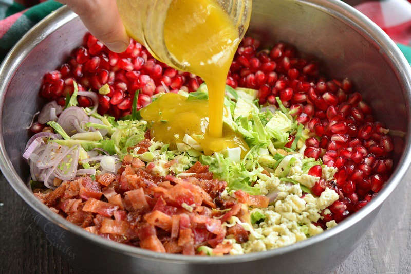 pouring mustard vinaigrette into salad in a metal bowl
