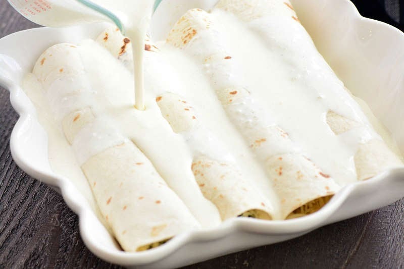 pouring sauce over enchiladas that ate in a casserole dish on a wood table