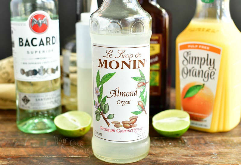 ingredients in bottle lined up with Almond Orgeat syrup bottle being on the foreground