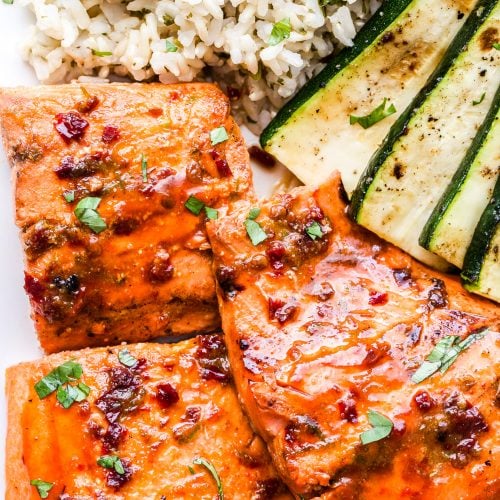 three pieces of salmon on a plate with rice and zucchini slices