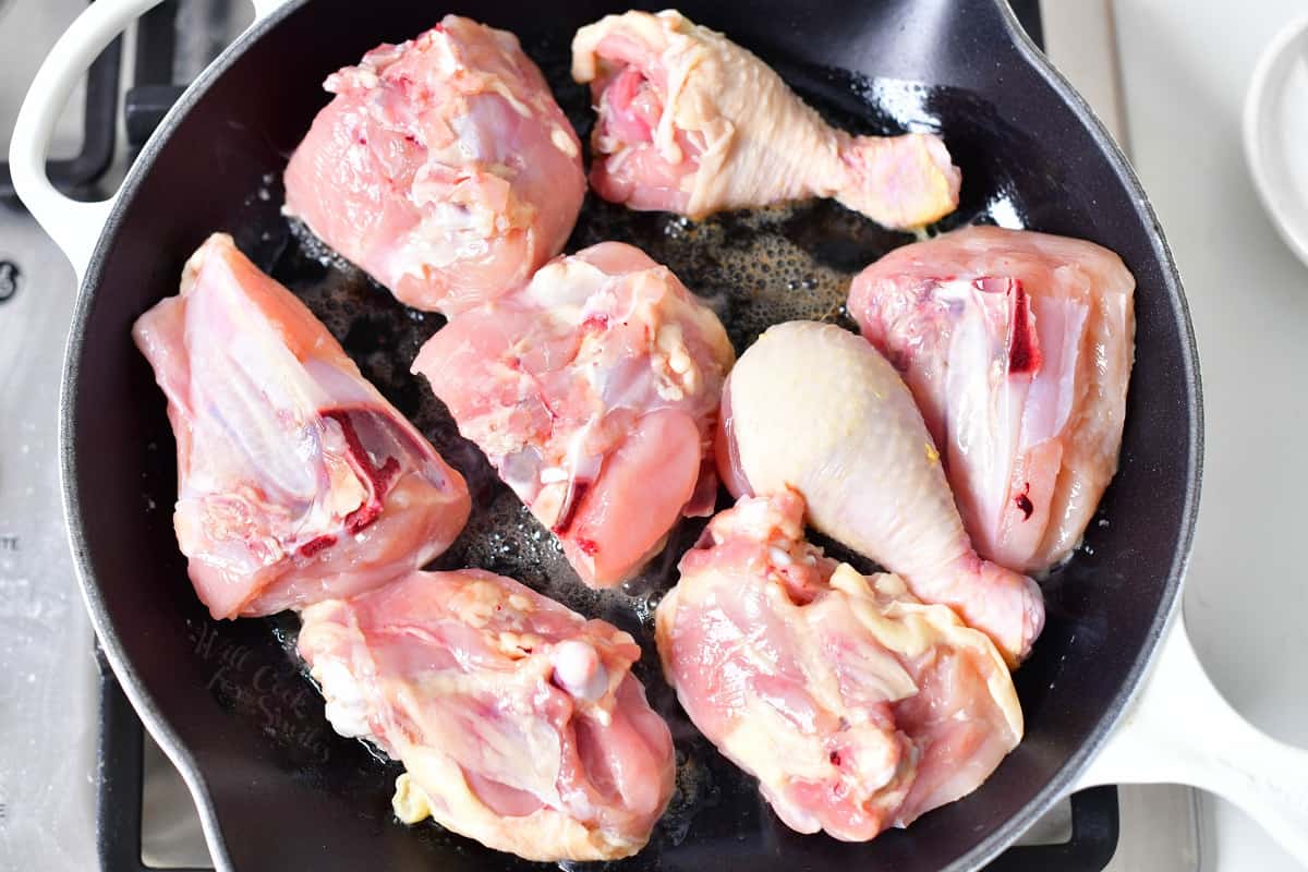 wight raw pieces of bone-in chicken in frying pan of oil.