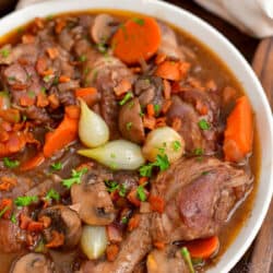 closeup: cooked French chicken recipe in a white bowl with a wooden spoon and cloth napkin
