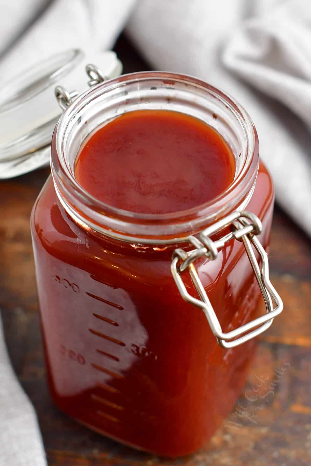 An open mason jar is filled with red BBQ sauce.