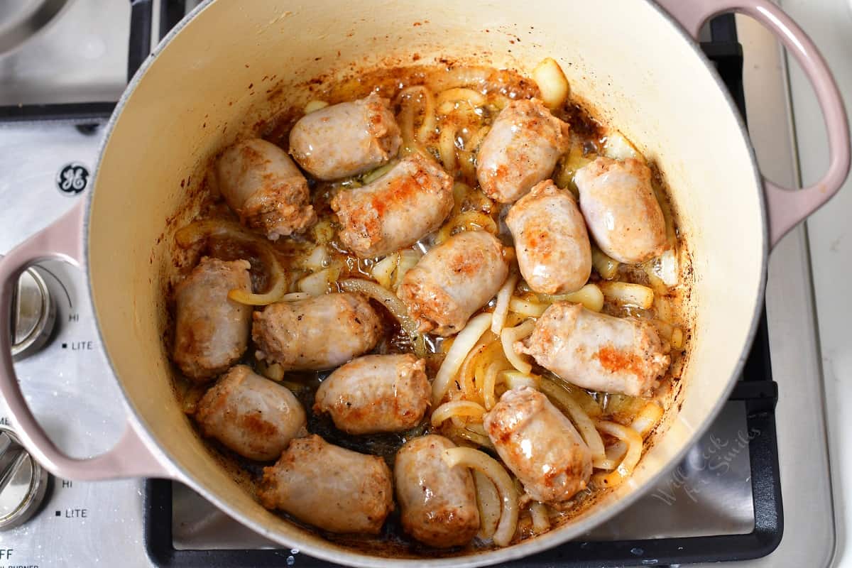 Sausage pieces and onion slices are being cooked in a large pot.