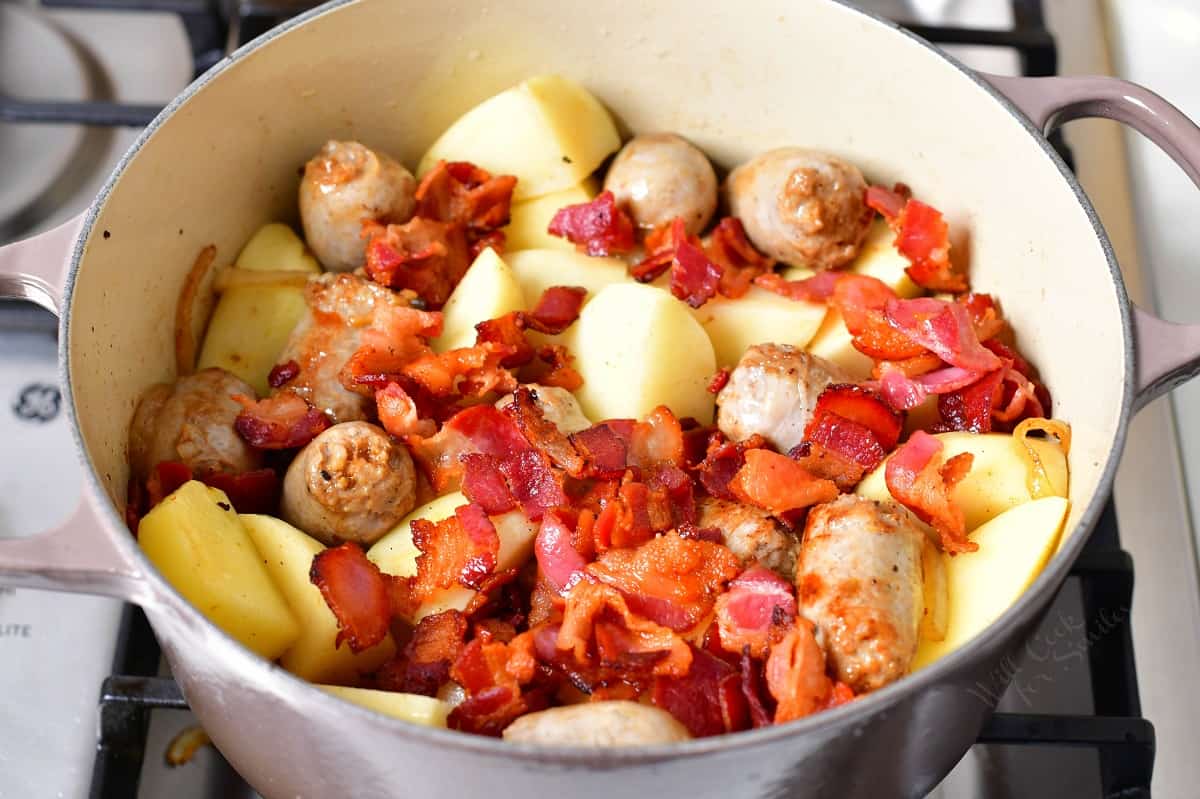 Bacon and potatoes have been added to the pot, placed on top of sausages and onions.