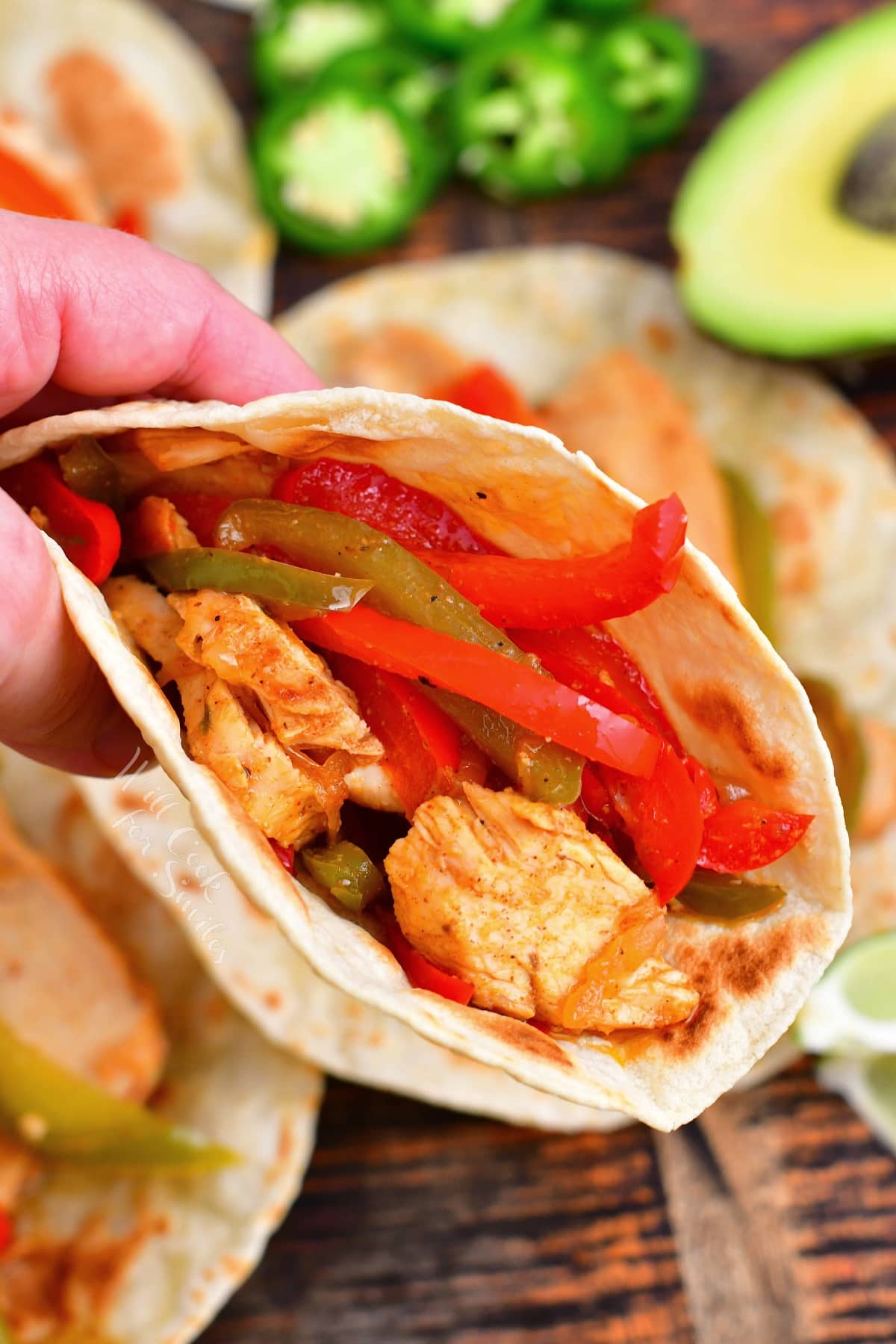 A hand is holding up a perfectly made chicken fajita.