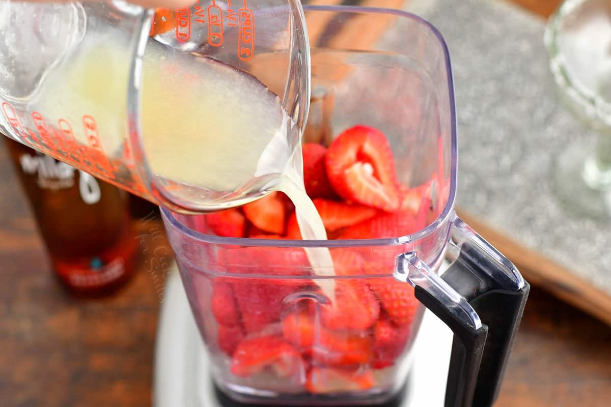 Liquid is being poured into a blender of strawberries.