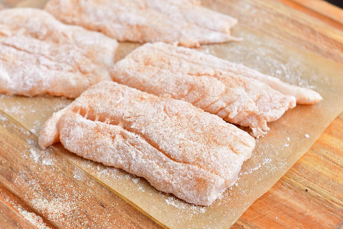 Uncooked cod is coated in flour and placed on a sheet of parchment paper.