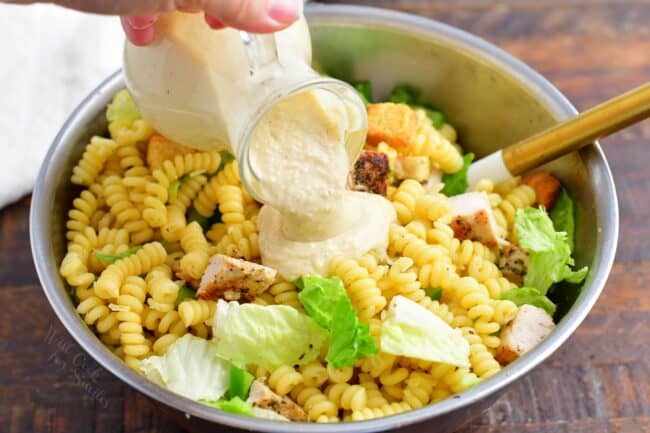 Dressing is being poured on top of pasta salad.