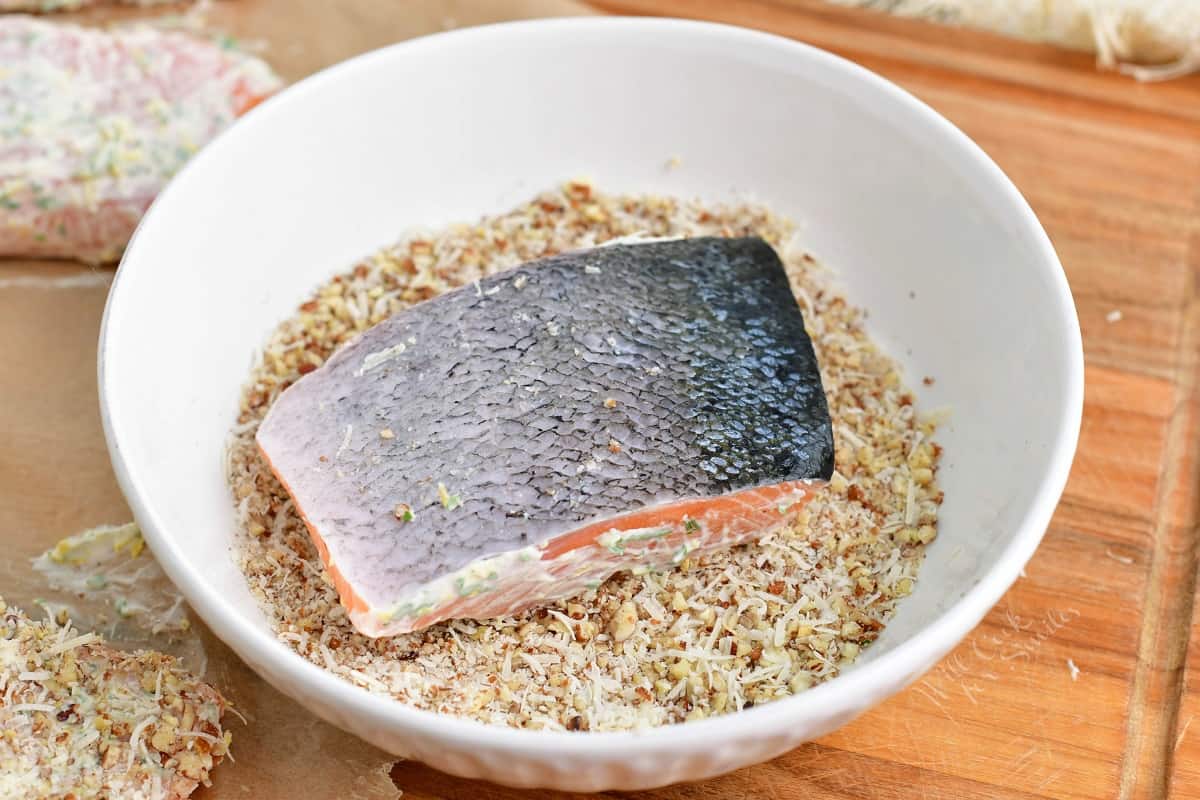 A salmon filet is dipped into pecans and parmesan.