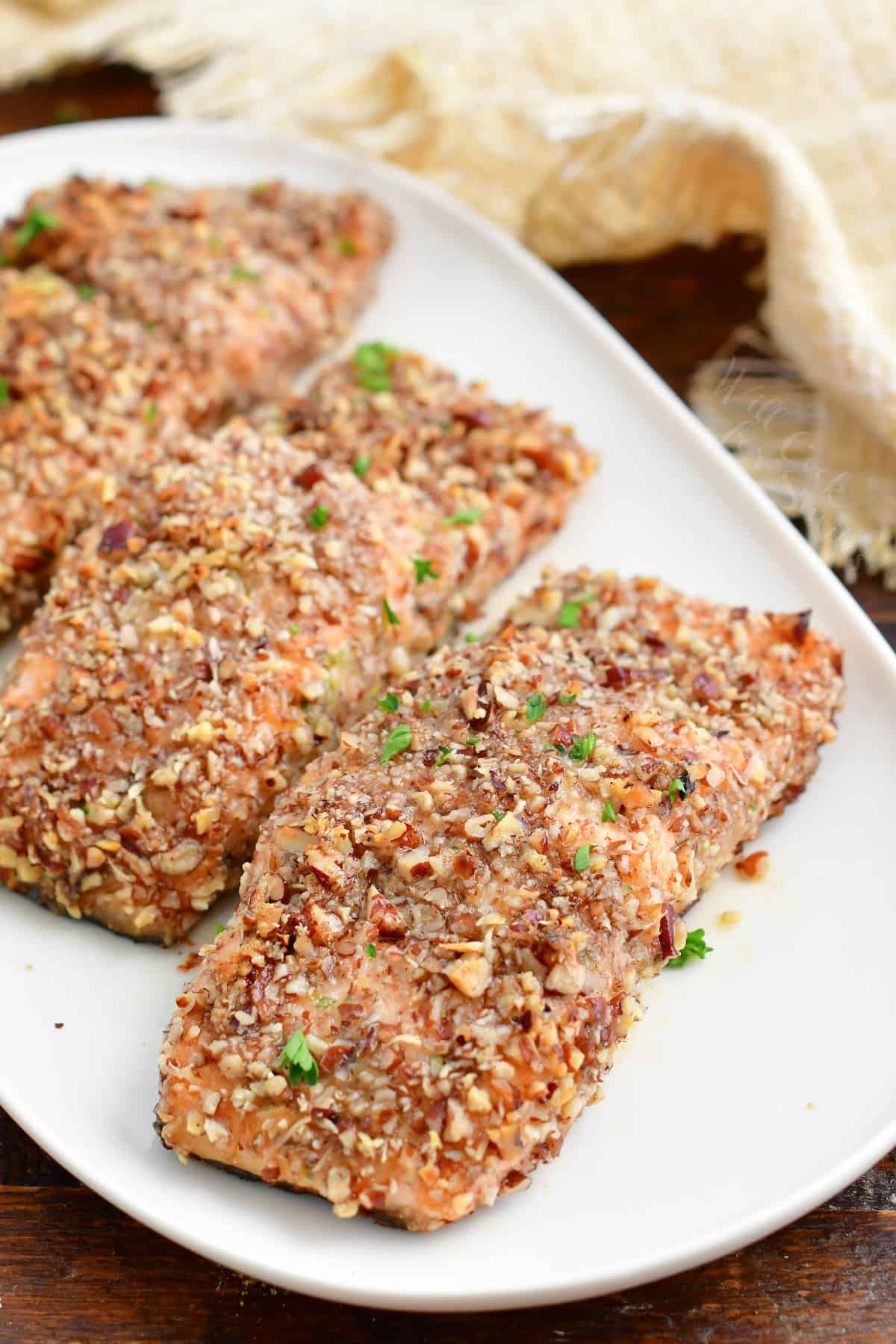 Pecan crusted salmon filets are ready to eat on a white plate.