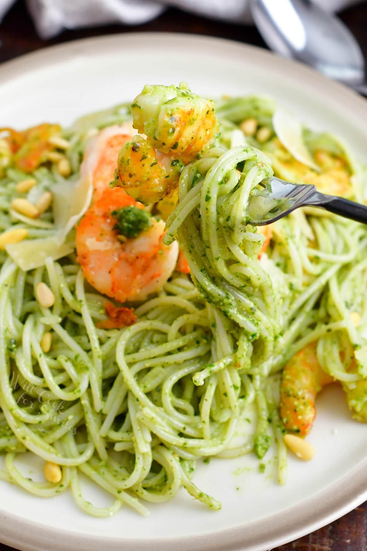 A fork is twirling a bite sized portion of pesto pasta.