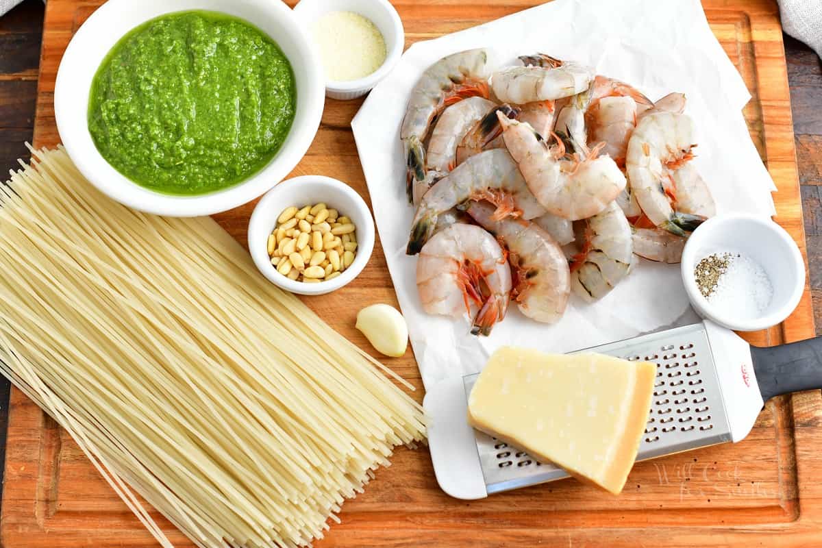 The ingredients for shrimp pesto pasta are placed on a wooden cutting board.