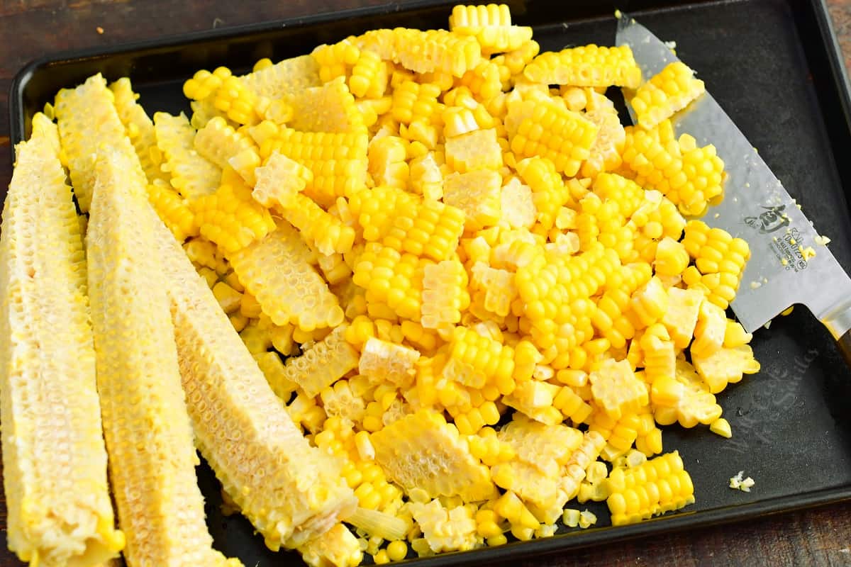 Corn kernels that were cut off of the cob on a baking sheet with a knife next to them.