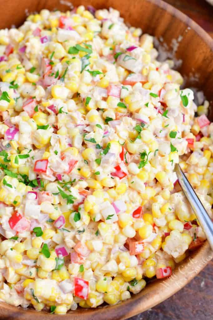 A large silver spoon is stuck on the side of a bowl filled with creamy corn salad.
