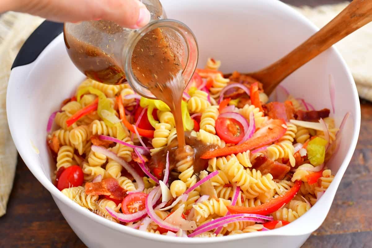 Dressing is being poured on top of a pasta salad.