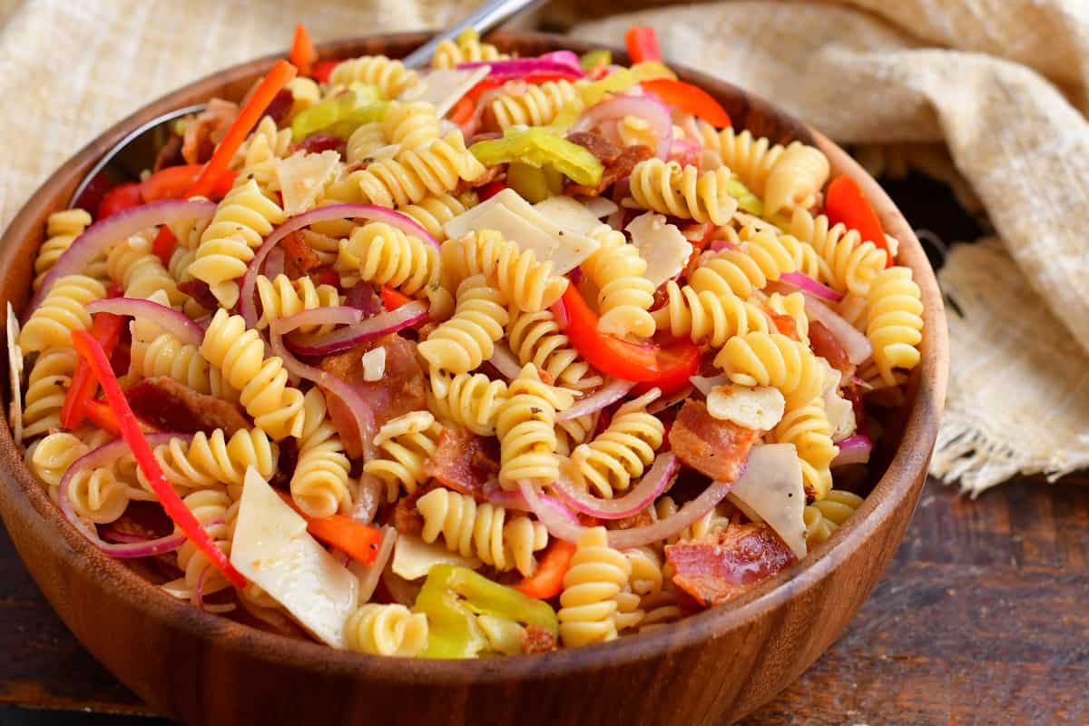 A pasta salad is presented in a large wooden bowl, ready to be served.