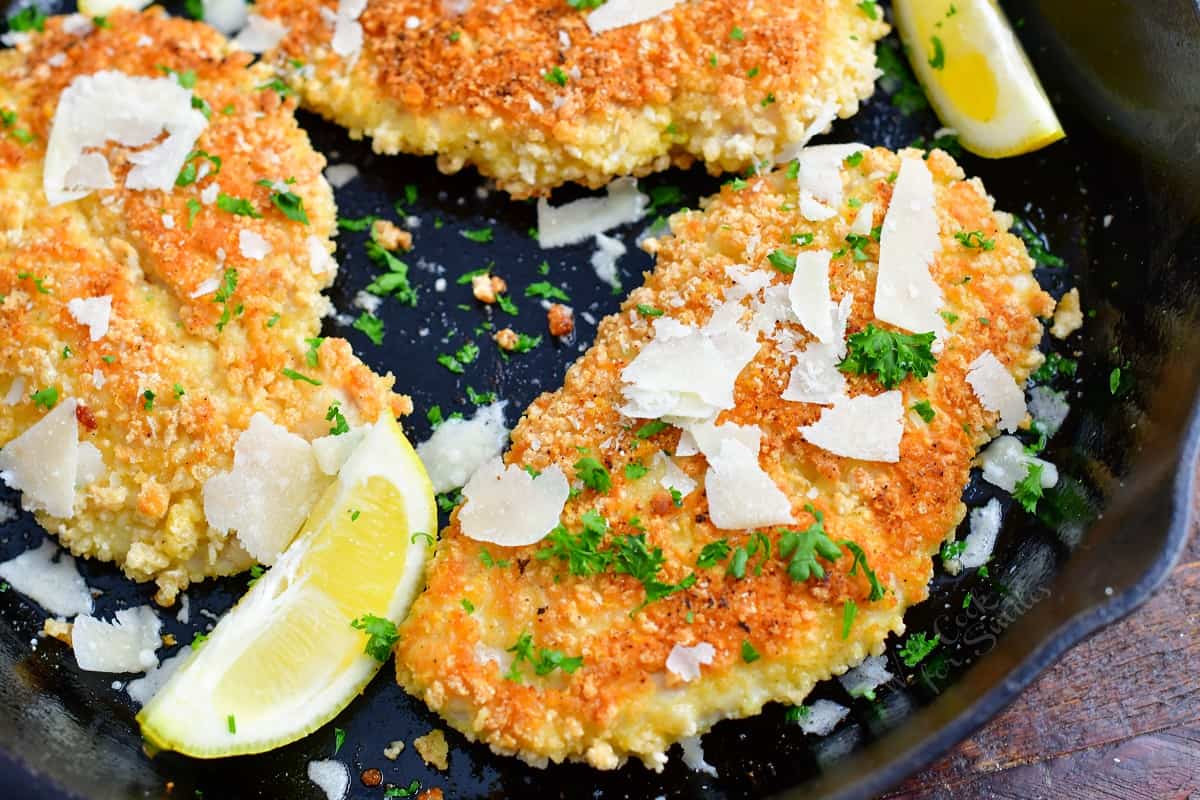 Lemon wedges, parmesan and parsley are in a pan with cooked chicken.
