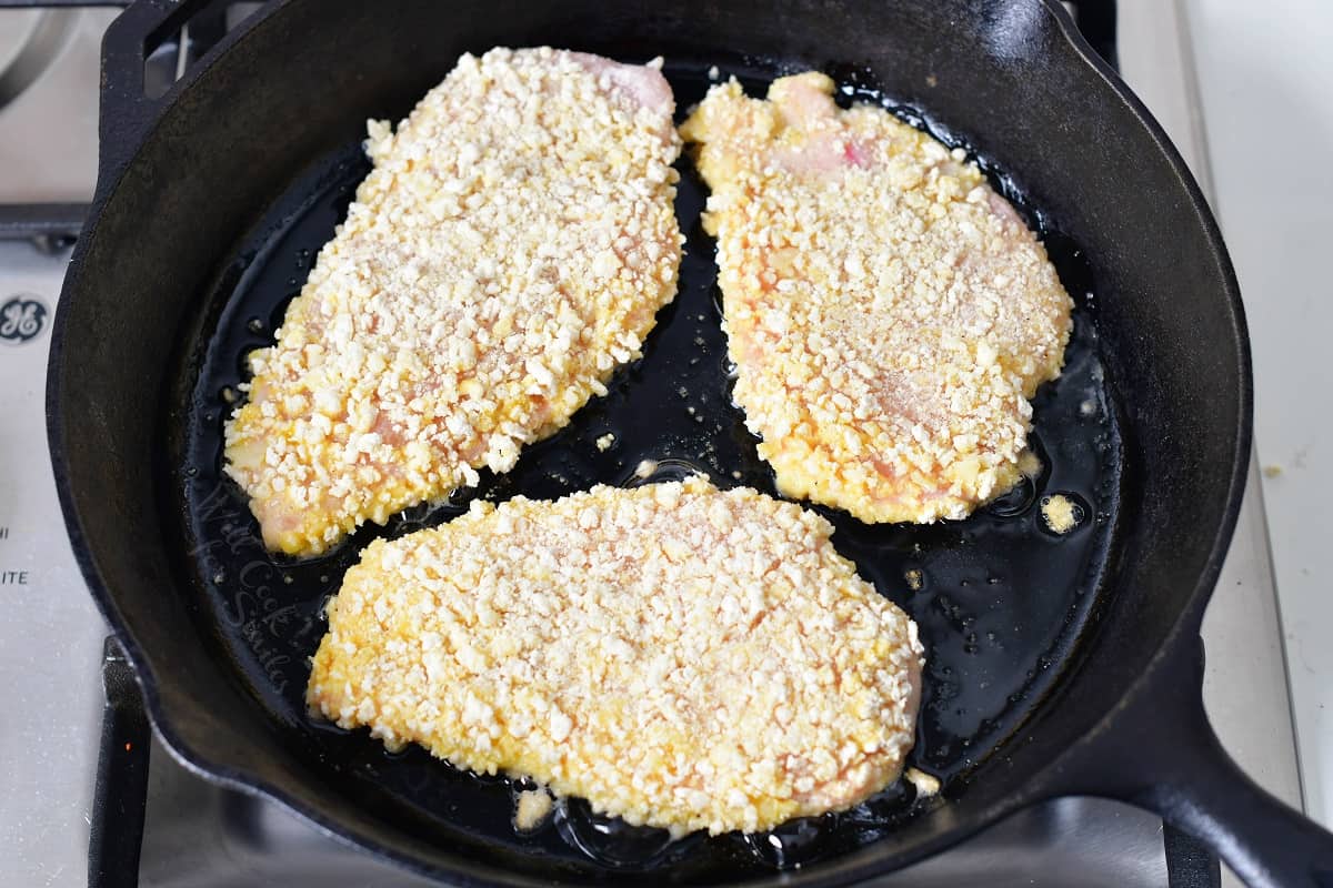Three chicken breasts are being cooked in a black pan.